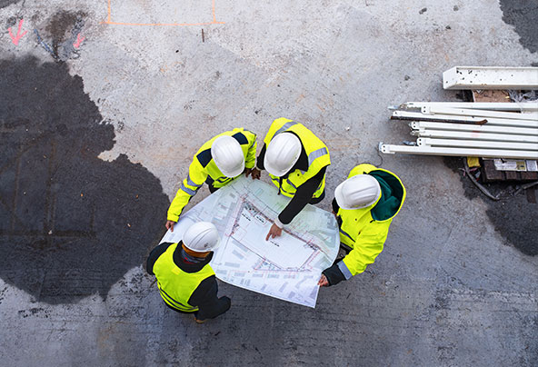 Personen mit Bauplan auf Baustelle von oben